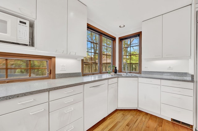 kitchen with white microwave, light wood-type flooring, white cabinetry, and a sink