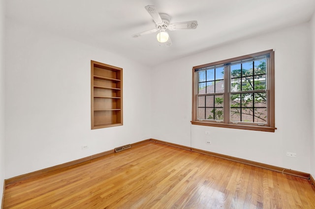 spare room featuring baseboards, light wood-type flooring, built in features, and a ceiling fan