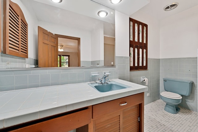 bathroom featuring toilet, tile patterned floors, vanity, wainscoting, and tile walls