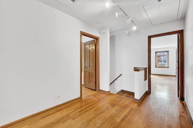 spare room with attic access, light wood-style flooring, baseboards, and track lighting