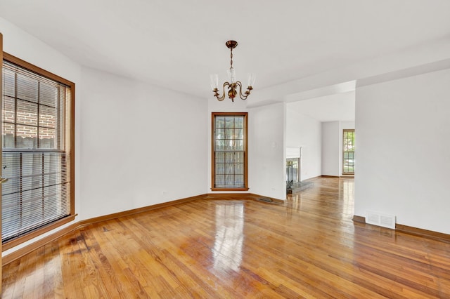 unfurnished room with a chandelier, light wood-style flooring, and baseboards