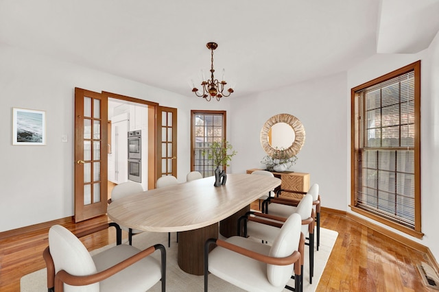 dining area featuring a chandelier, light wood-style flooring, french doors, and baseboards