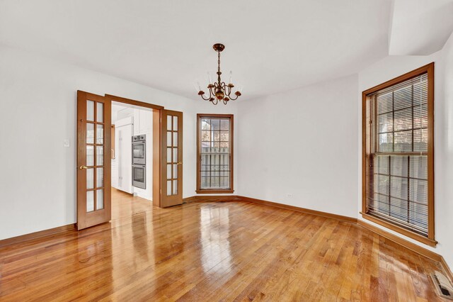 unfurnished room featuring a chandelier, light wood-style flooring, baseboards, and french doors