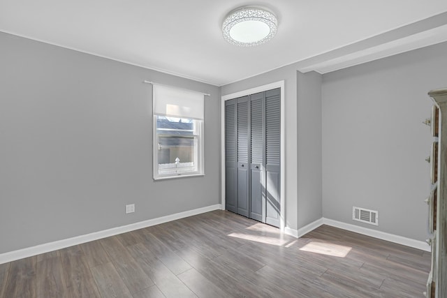 unfurnished bedroom featuring wood finished floors, baseboards, a closet, and visible vents