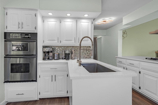 kitchen with tasteful backsplash, a peninsula, white cabinetry, stainless steel double oven, and a sink