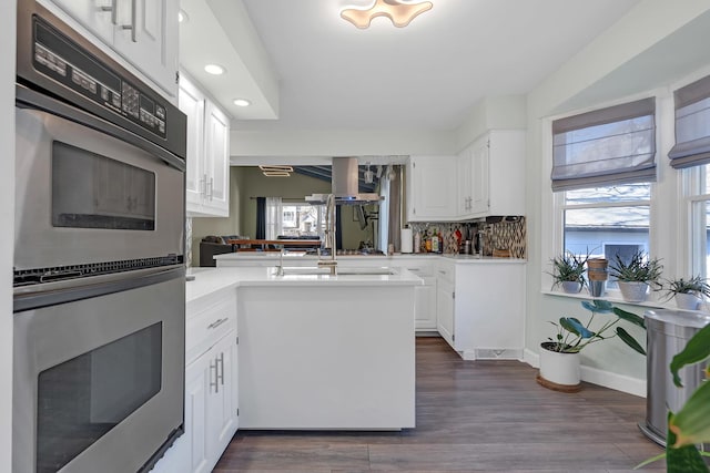 kitchen with a peninsula, stainless steel double oven, light countertops, and recessed lighting