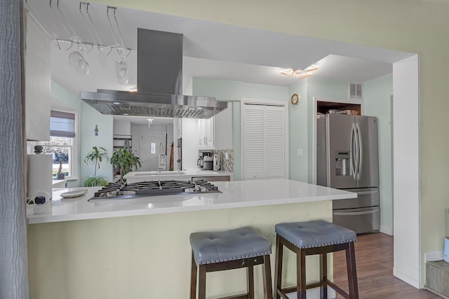 kitchen with white cabinets, visible vents, stainless steel appliances, island range hood, and a breakfast bar area