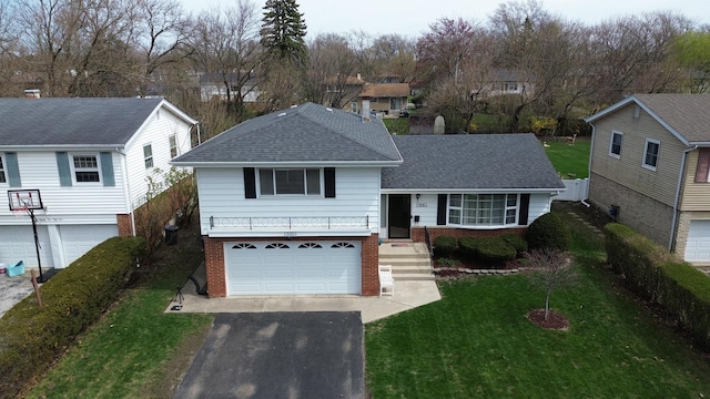 tri-level home with roof with shingles, a front yard, brick siding, an attached garage, and driveway