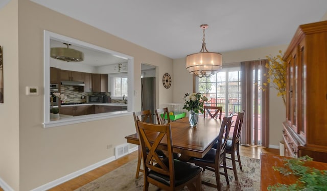 dining space with light wood-style flooring, an inviting chandelier, baseboards, and visible vents