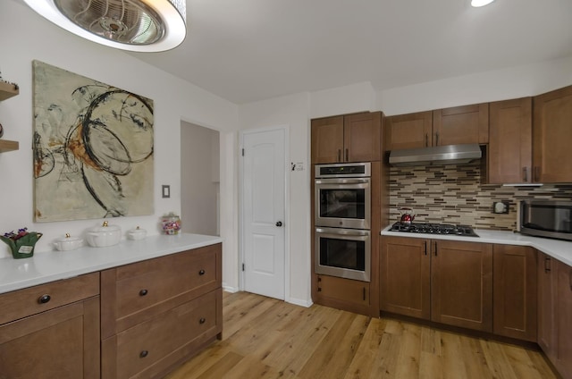 kitchen with tasteful backsplash, light countertops, under cabinet range hood, stainless steel appliances, and light wood finished floors