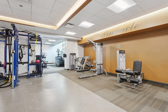 exercise room featuring carpet floors, a paneled ceiling, and baseboards