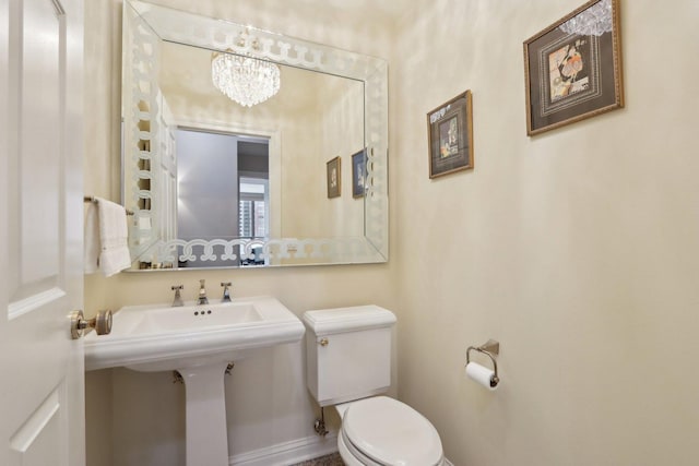 half bath with toilet, baseboards, and an inviting chandelier