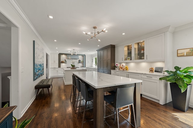 kitchen with a breakfast bar area, a notable chandelier, ornamental molding, and glass insert cabinets