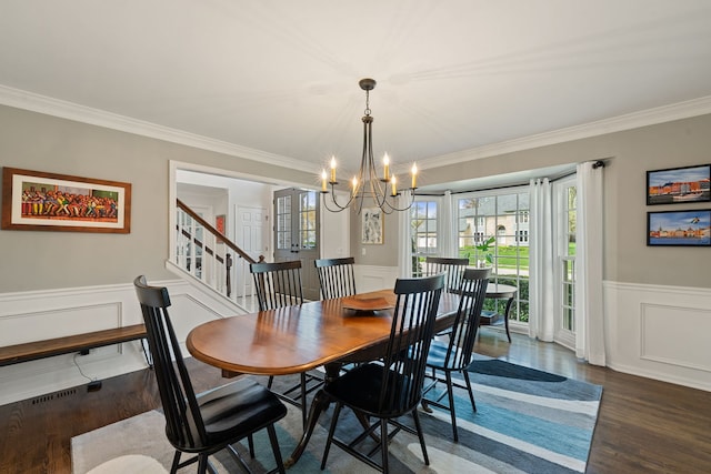 dining area with crown molding, an inviting chandelier, wood finished floors, a decorative wall, and a wainscoted wall