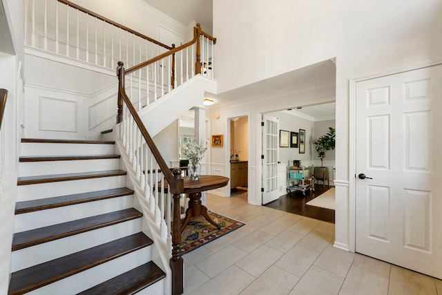 entryway featuring light tile patterned floors, a wainscoted wall, ornamental molding, a high ceiling, and stairs