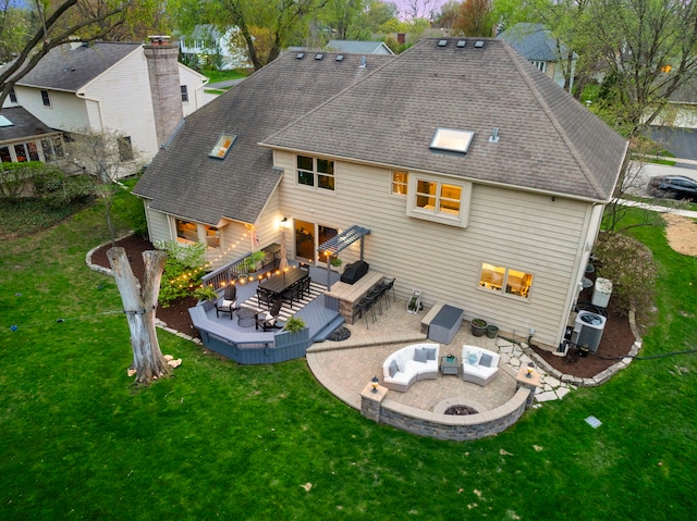 rear view of property with a lawn, a wooden deck, central AC, an outdoor living space with a fire pit, and a shingled roof