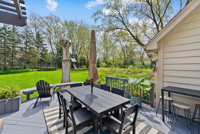 wooden deck featuring a lawn, fence, outdoor dining area, and a playground