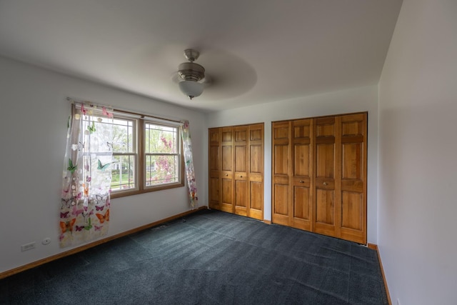 unfurnished bedroom with dark colored carpet, multiple closets, ceiling fan, and baseboards