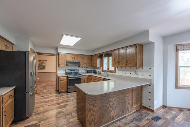 kitchen with dark wood-style flooring, stainless steel appliances, a peninsula, and under cabinet range hood