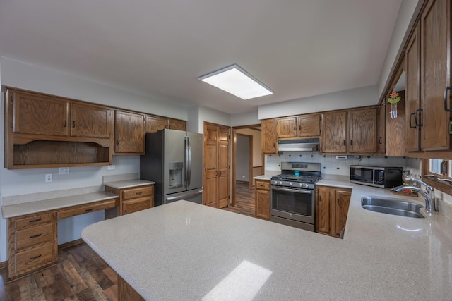kitchen featuring a sink, light countertops, stainless steel appliances, a peninsula, and under cabinet range hood
