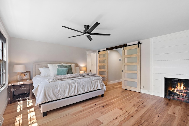 506 Aberdeen Rd, Frankfort, IL 60423 - bedroom with a barn door, light wood finished floors, a warm lit fireplace, baseboards, and a ceiling fan