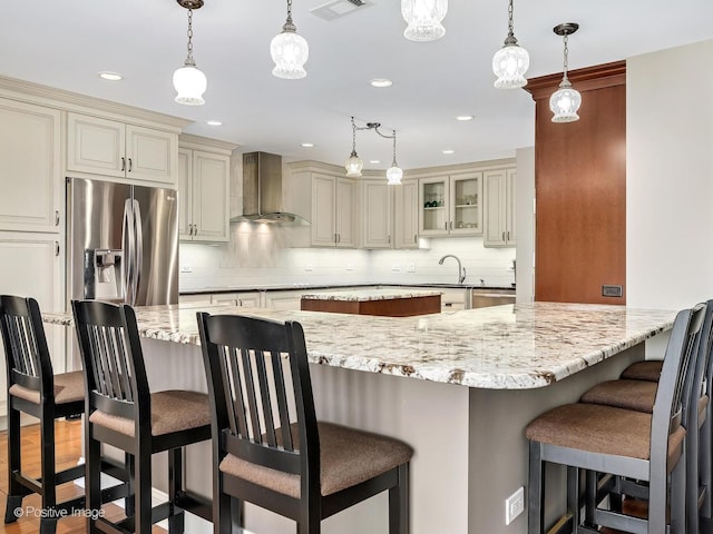 kitchen with light stone countertops, stainless steel appliances, cream cabinetry, tasteful backsplash, and wall chimney range hood