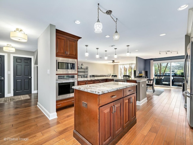 kitchen featuring light wood-style flooring, appliances with stainless steel finishes, a center island, decorative light fixtures, and a peninsula