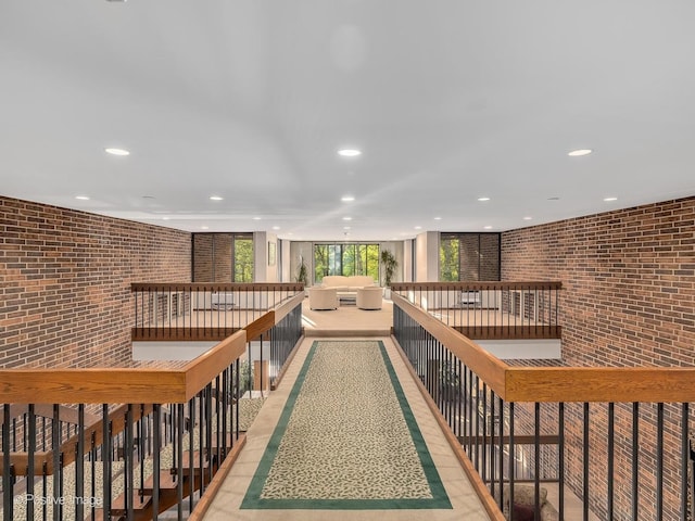 corridor featuring an upstairs landing, brick wall, and recessed lighting