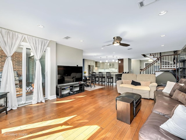 living room featuring stairway, visible vents, ceiling fan, and light wood-style flooring