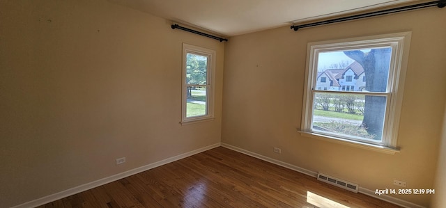 unfurnished room with dark wood-style floors, a wealth of natural light, visible vents, and baseboards
