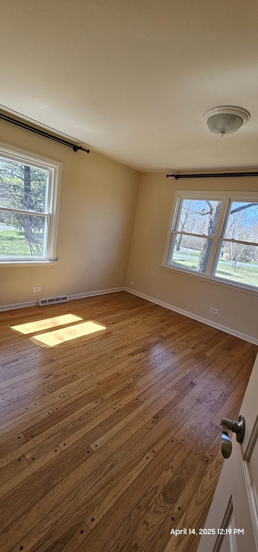 unfurnished room featuring wood-type flooring, baseboards, and visible vents