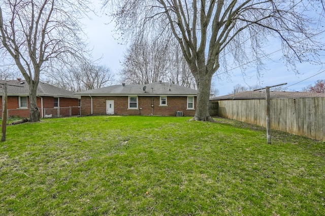 rear view of property featuring brick siding, a fenced backyard, and a lawn