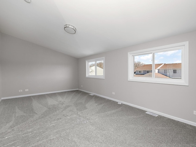 carpeted spare room with visible vents, baseboards, and lofted ceiling