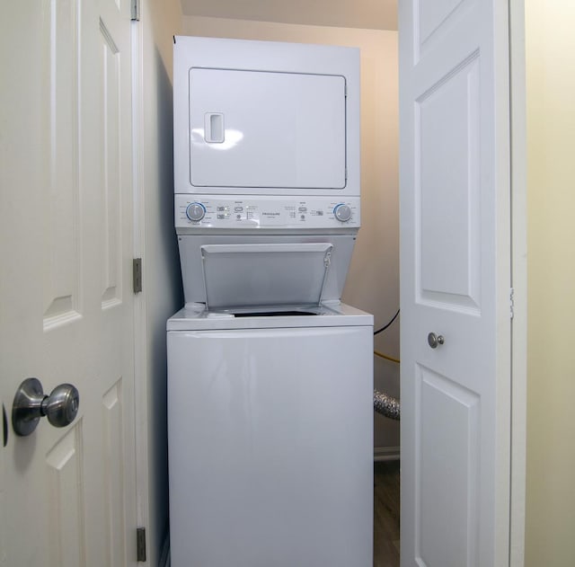 laundry room with wood finished floors, stacked washer / dryer, and laundry area