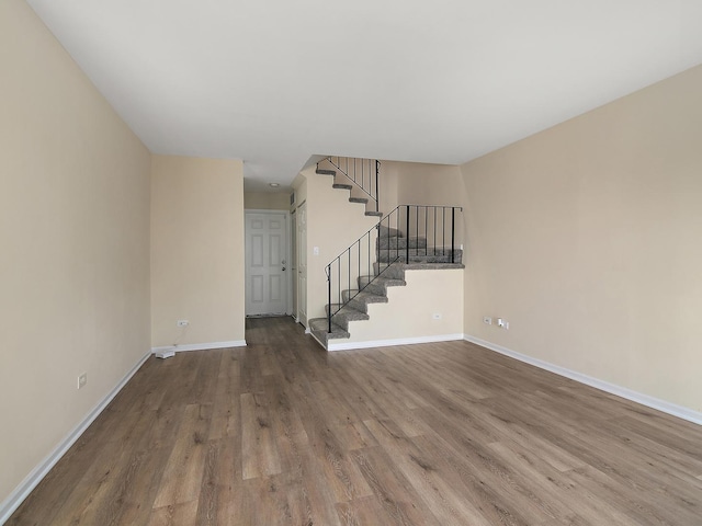 unfurnished living room featuring wood finished floors, baseboards, and stairway