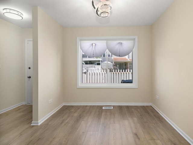 spare room featuring visible vents, baseboards, an inviting chandelier, and wood finished floors