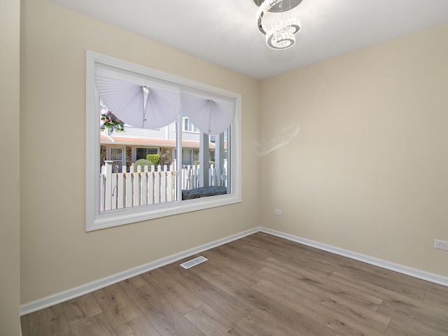 unfurnished room with a chandelier, visible vents, baseboards, and wood finished floors