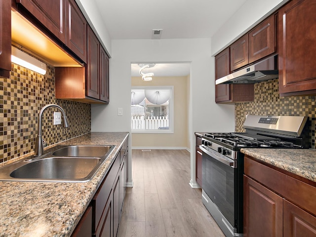 kitchen featuring baseboards, a sink, under cabinet range hood, gas stove, and light wood-style flooring