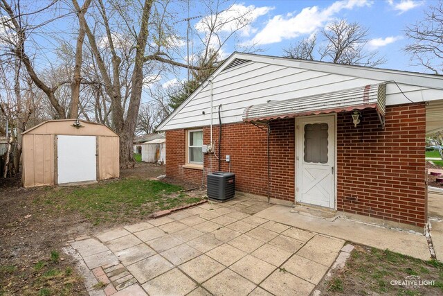 back of property with a storage unit, an outbuilding, central AC, brick siding, and a patio