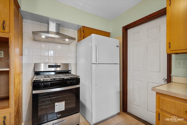 kitchen featuring light tile patterned floors, freestanding refrigerator, wall chimney range hood, light countertops, and stainless steel gas stove