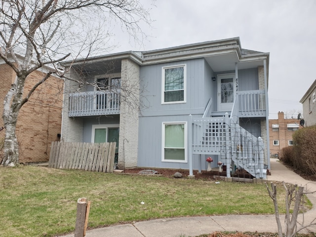 rear view of house featuring a lawn, a balcony, stairway, and fence