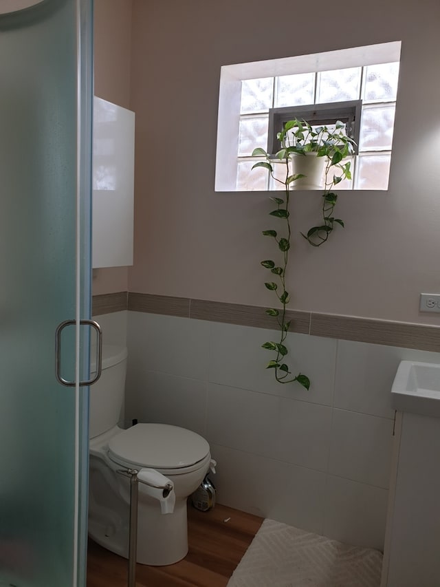 bathroom with tile walls, wood finished floors, a stall shower, and toilet