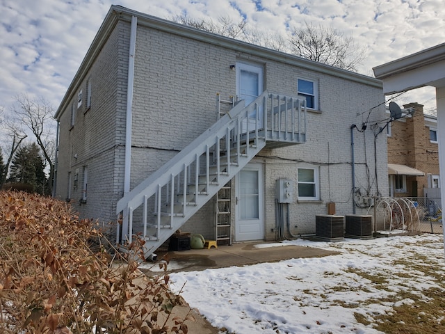 snow covered property featuring brick siding, fence, and cooling unit