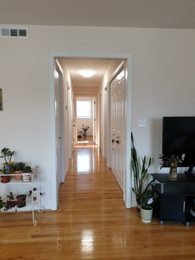 corridor with light wood-style floors, visible vents, and baseboards