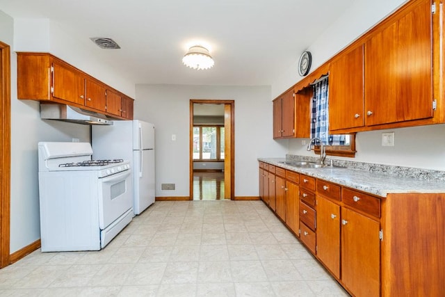 kitchen featuring white appliances, baseboards, under cabinet range hood, brown cabinets, and a sink