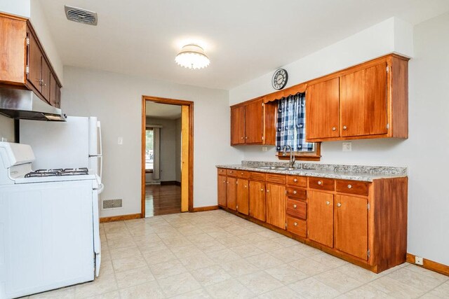 kitchen with baseboards, brown cabinets, under cabinet range hood, and white range with gas cooktop