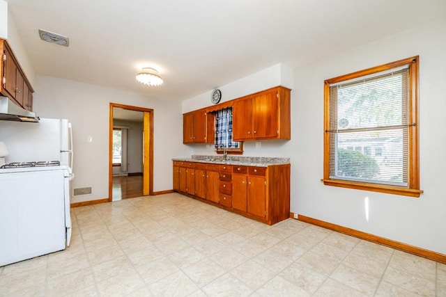 kitchen featuring a sink, stove, baseboards, under cabinet range hood, and visible vents