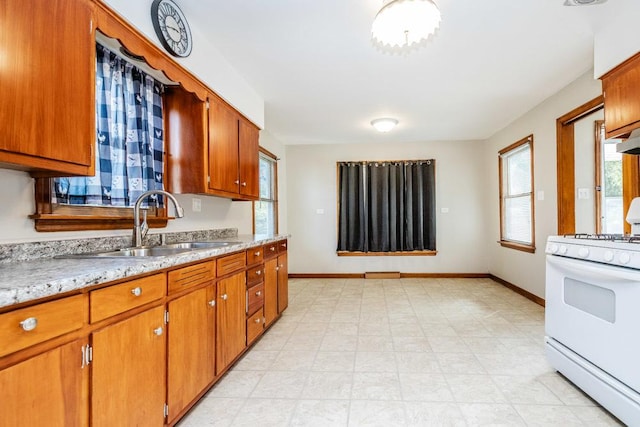 kitchen with a sink, baseboards, white gas range oven, and brown cabinetry