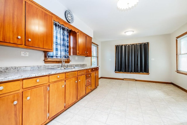 kitchen with baseboards, brown cabinetry, and a sink