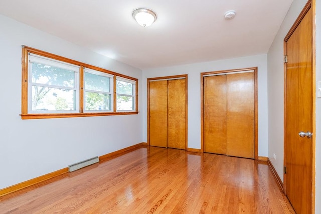 unfurnished bedroom featuring light wood-style floors, a baseboard radiator, baseboards, and two closets